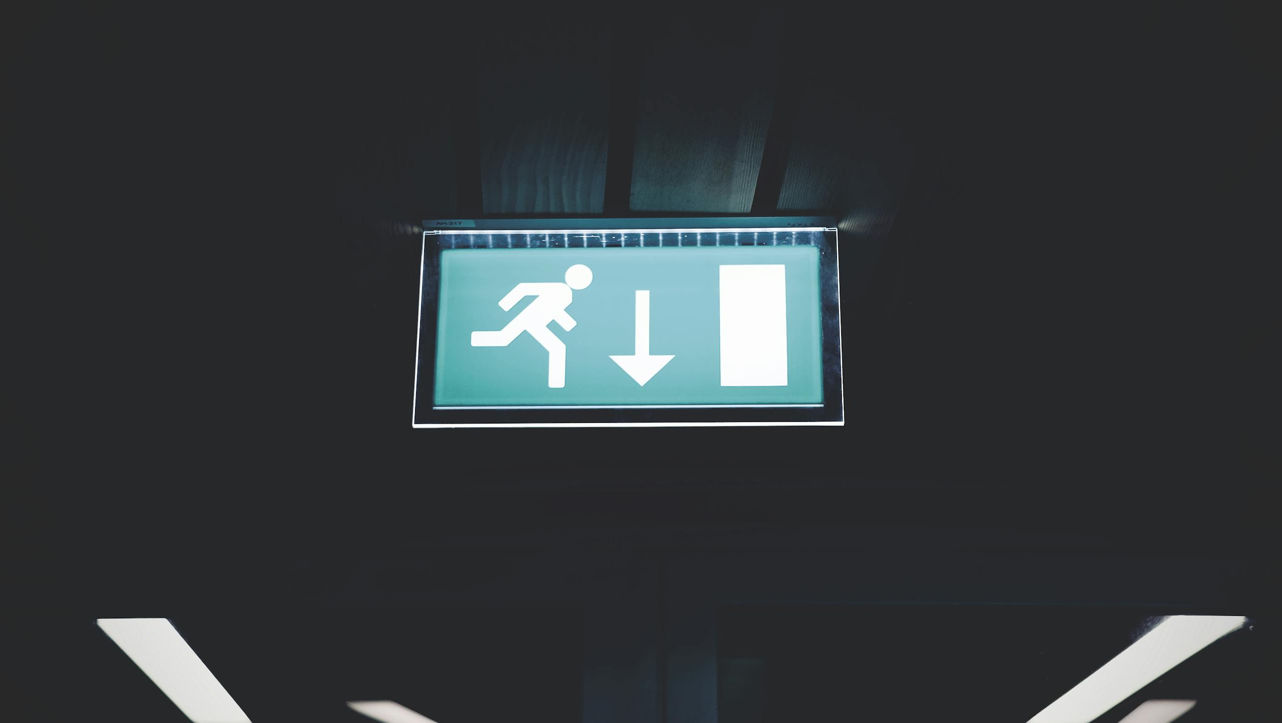 Brightly lit emergency exit sign with arrow indicating direction, set against a dark backdrop.